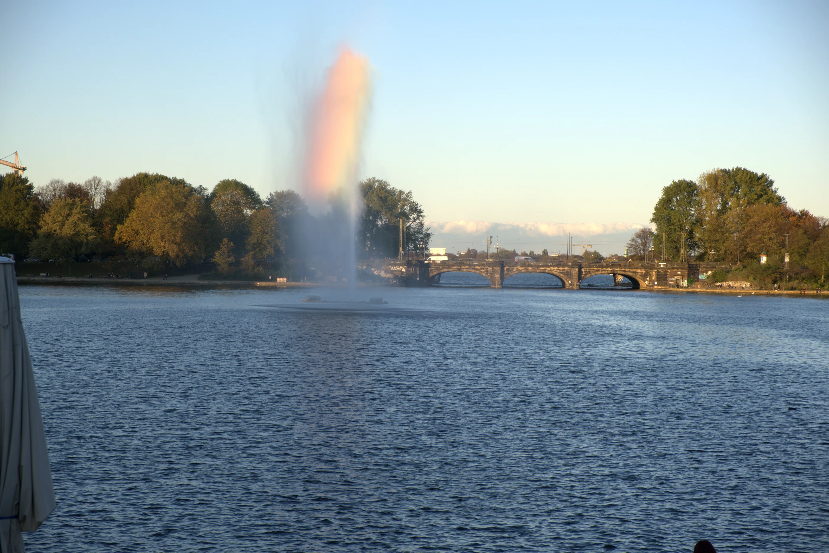 Alsterfontäne im Abendlicht mit Regenbogen und Lombardsbrücke